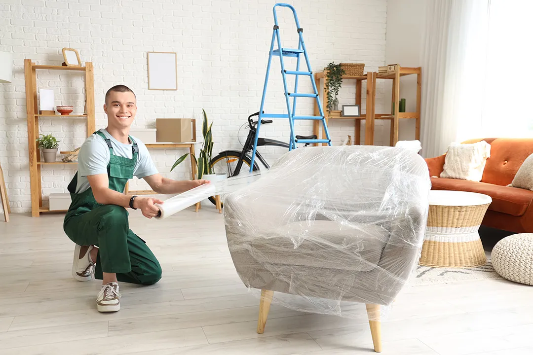 Umzugsmitarbeiter verpackt einen Sessel mit Stretchfolie